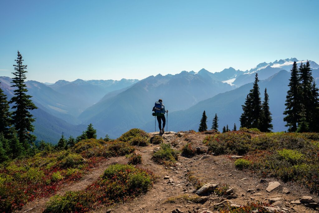 Woman backpacking in the Olympic mountains in Washington stands facing the glacial mountains.